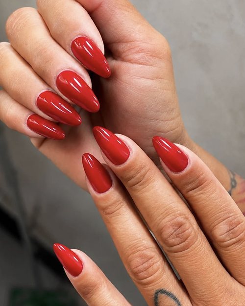 Mani con semipermanente rosso brillante su unghie a mandorla